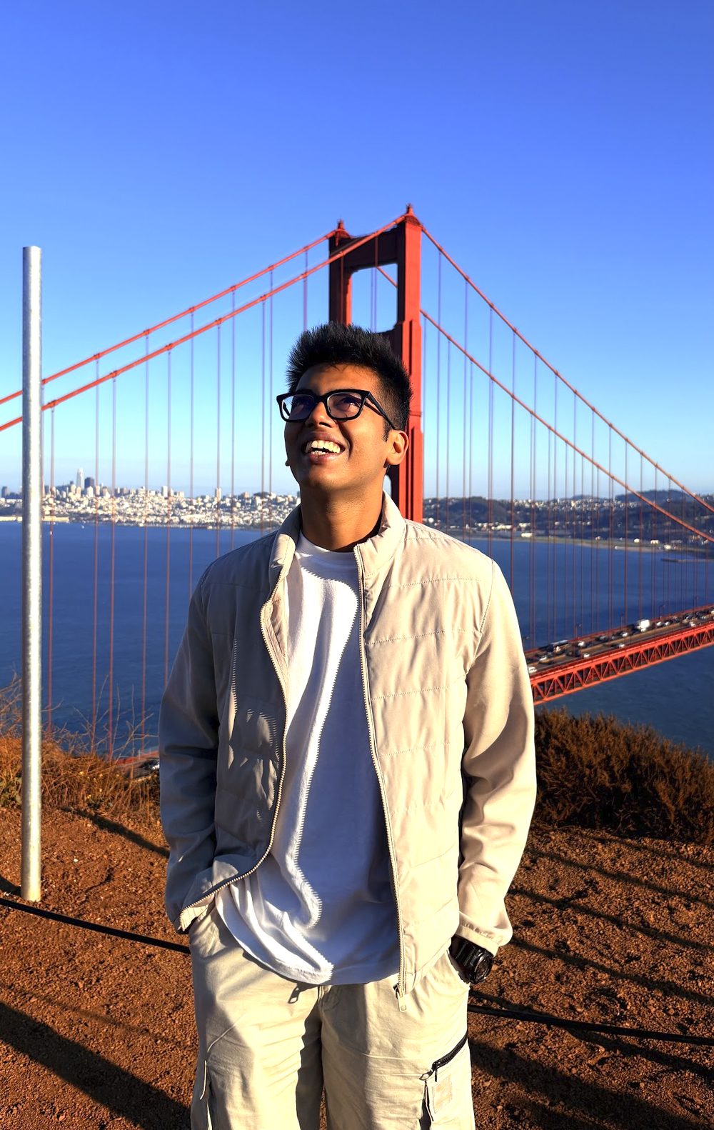 Ishaan Godha smiling and looking up in front of the Golden Gate Bridge